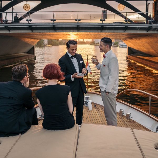 Gäste auf dem Vordeck der Motoryacht Fitzgerald vor der Oberbaumbrücke bei Sonnenuntergang